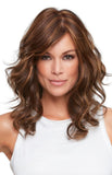 Woman with thinning hair is covering her hair in a synthetic wavy wig in the style called Alexis 